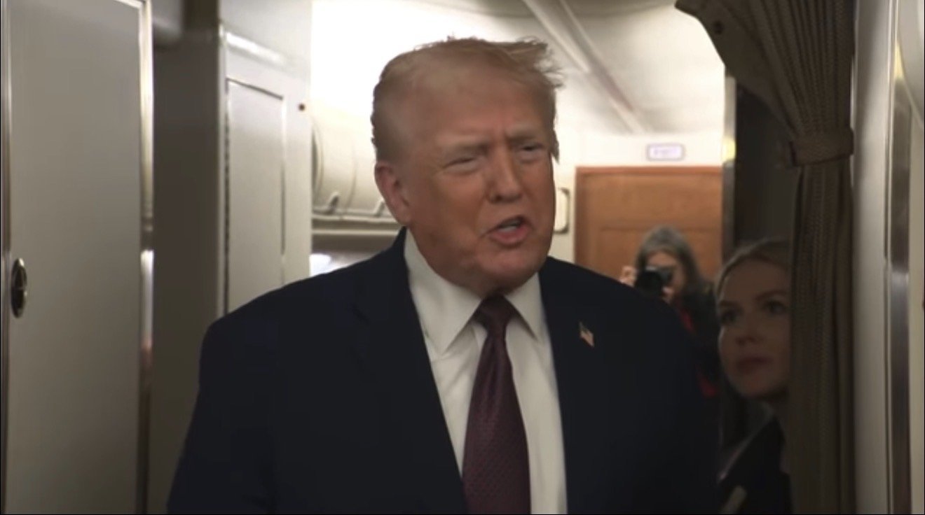 Donald Trump speaking onboard an aircraft, engaging with staff and media in a candid moment.