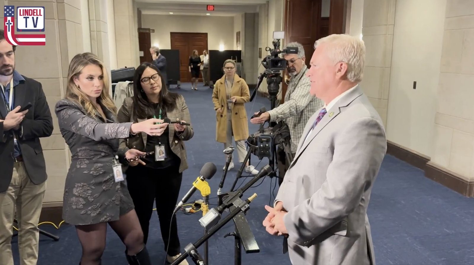 Press conference scene with reporters interviewing a politician, capturing media engagement and professional interactions in a government building.