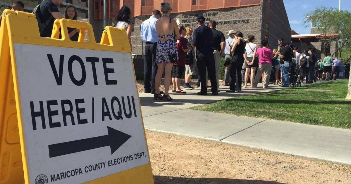 Voters lined up outside a polling station with a sign directing them to vote, emphasizing civic engagement in the electoral process.