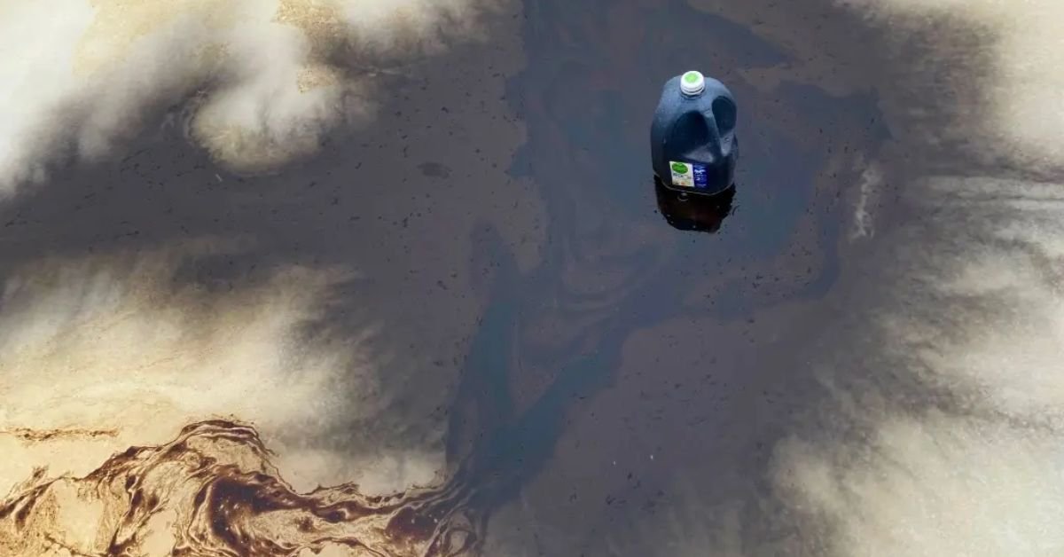 A plastic jug floats on a dark, oily surface, highlighting environmental pollution and its impact on water quality.