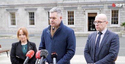 Press conference featuring three speakers addressing the media outside a government building, with microphones and press equipment visible.