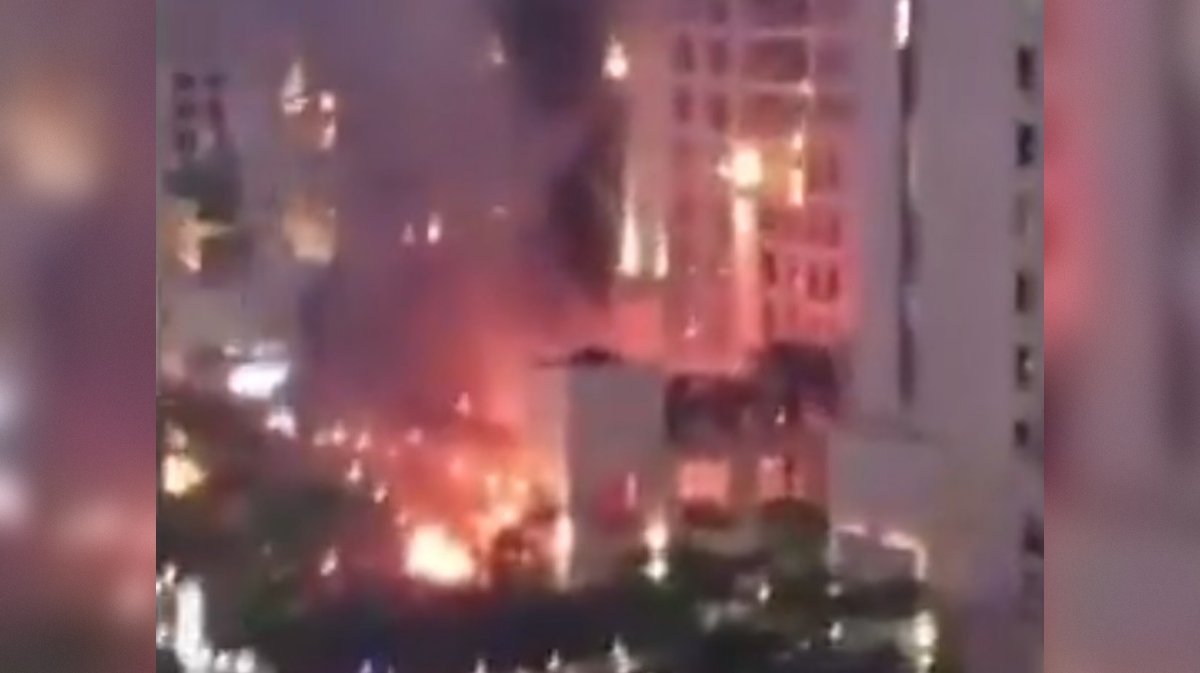 A large fire engulfs a building at night, with flames and smoke rising high into the air, creating a dramatic scene.