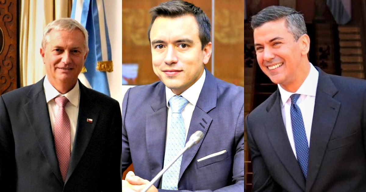 Three male politicians in formal attire, standing against a backdrop of flags and architectural elements, showcasing their professional demeanor and engagement in public service.