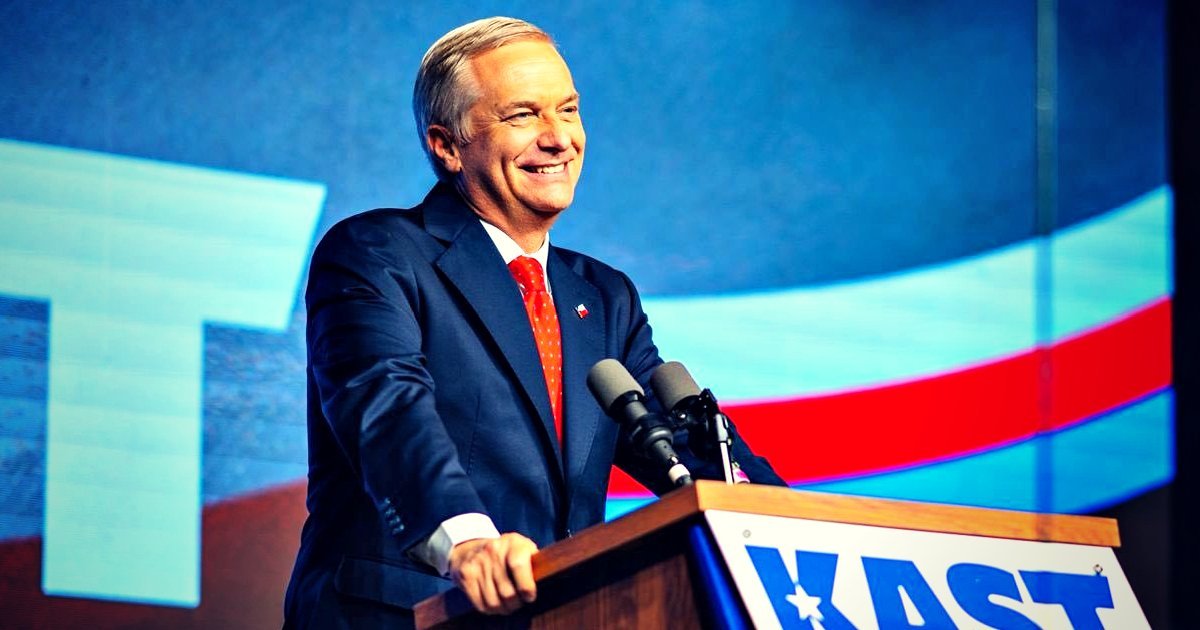 Smiling politician at a podium with microphones, promoting his campaign during an event with colorful background graphics.