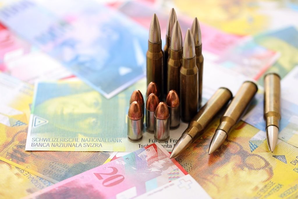 Assorted bullets arranged on a background of Swiss currency notes, symbolizing the contrast between money and weaponry.