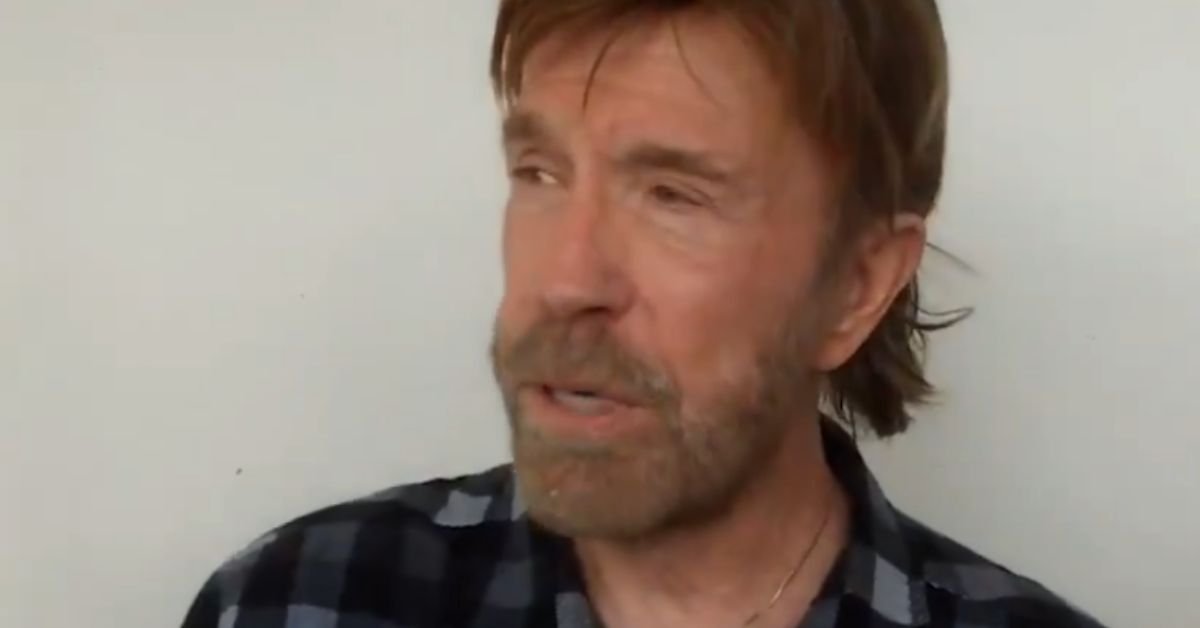 Actor Chuck Norris speaks in an interview, wearing a black and blue checkered shirt against a plain background.