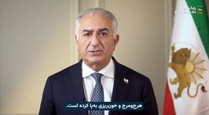 Reza Pahlavi delivers a speech, addressing political issues, with the Iranian flag in the background.