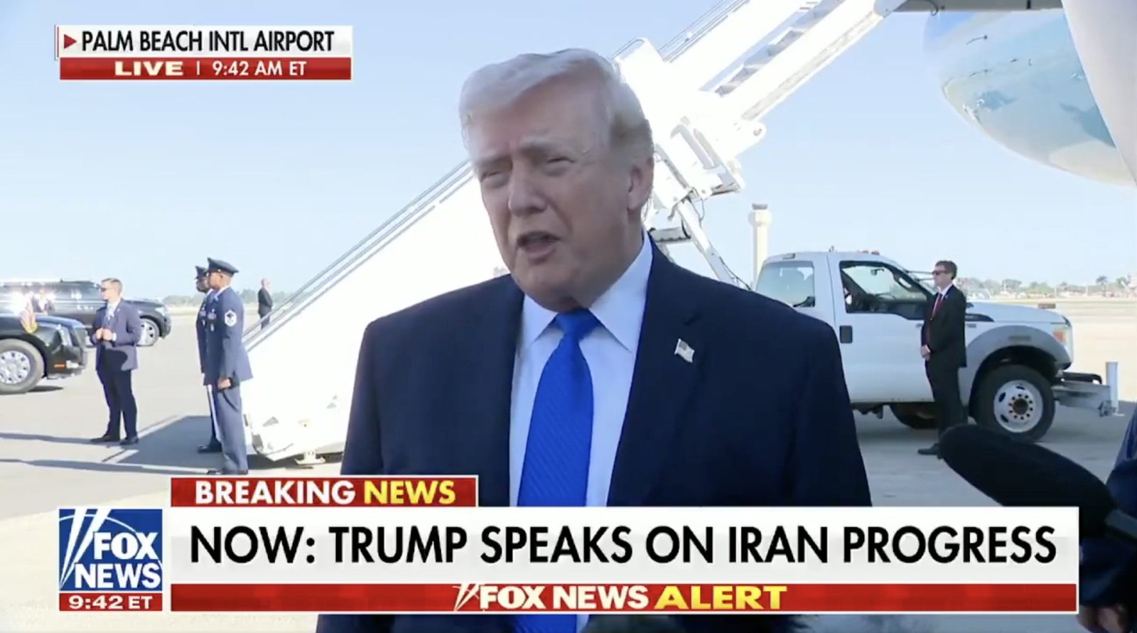 Donald Trump speaks at Palm Beach International Airport about progress on Iran, with security personnel and media present.