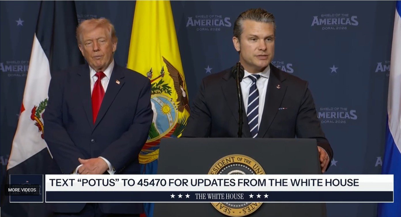 A speaker addresses an audience at the Shield of the Americas event, with flags in the background and a prominent White House seal displayed.